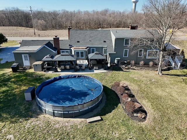 back of property featuring a covered pool, entry steps, a gazebo, a chimney, and a yard