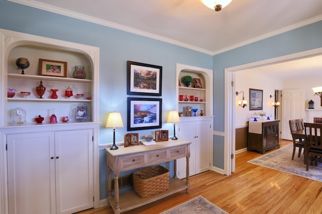 interior space featuring baseboards, built in shelves, light wood-style flooring, and ornamental molding