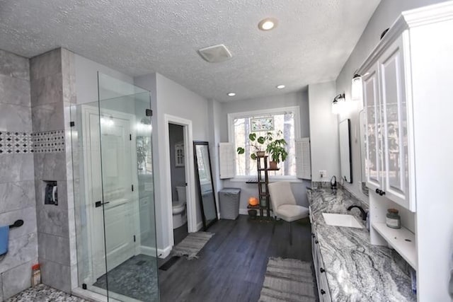 full bathroom featuring toilet, double vanity, a stall shower, wood finished floors, and a sink