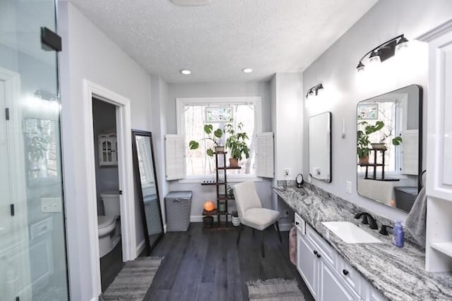 bathroom featuring toilet, a textured ceiling, wood finished floors, a freestanding bath, and vanity