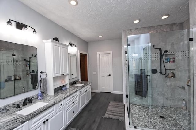 bathroom with double vanity, a shower stall, wood finished floors, and a sink