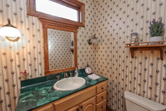 bathroom featuring toilet, vanity, and wallpapered walls