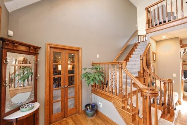 stairway featuring french doors, high vaulted ceiling, and wood finished floors