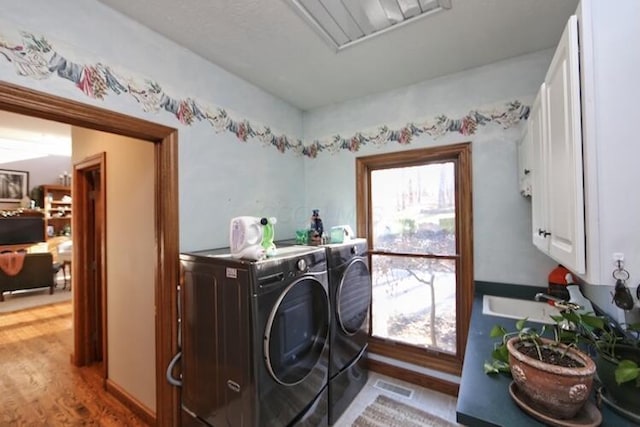 washroom featuring visible vents, washer and clothes dryer, wood finished floors, cabinet space, and a sink