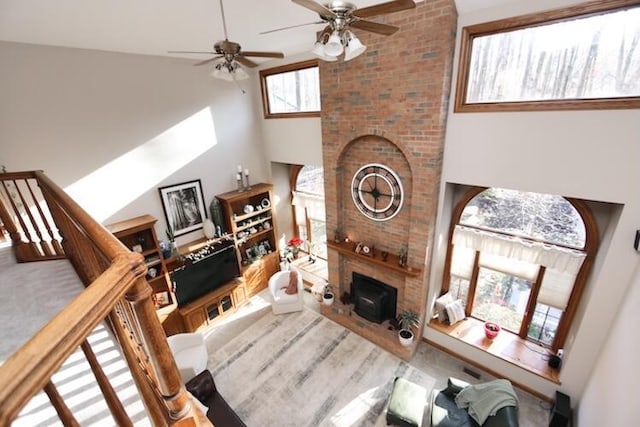 living area with stairway, a brick fireplace, a ceiling fan, and a towering ceiling