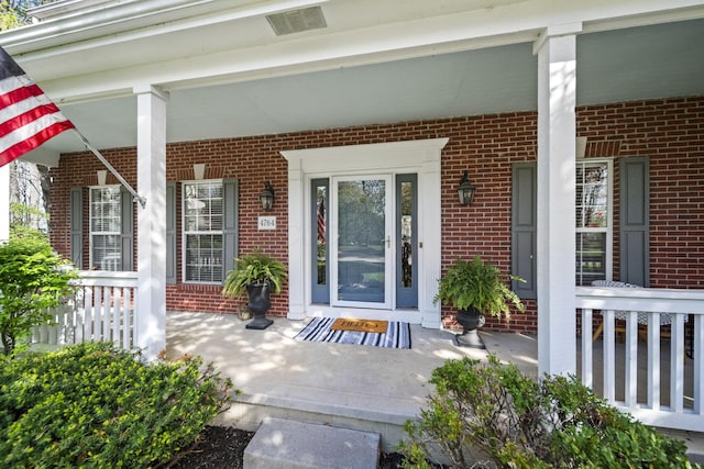 view of exterior entry featuring visible vents, covered porch, and brick siding