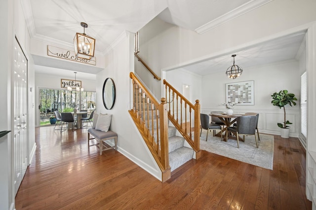 staircase with wood finished floors, crown molding, and a notable chandelier
