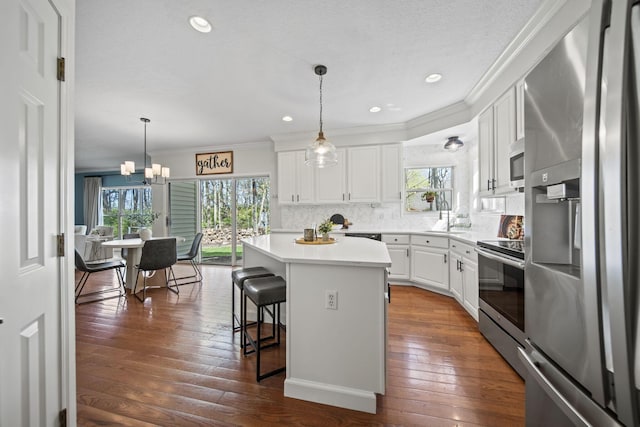 kitchen with crown molding, a breakfast bar area, a kitchen island, white cabinetry, and appliances with stainless steel finishes