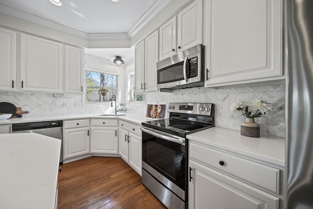 kitchen with a sink, white cabinetry, light countertops, ornamental molding, and appliances with stainless steel finishes