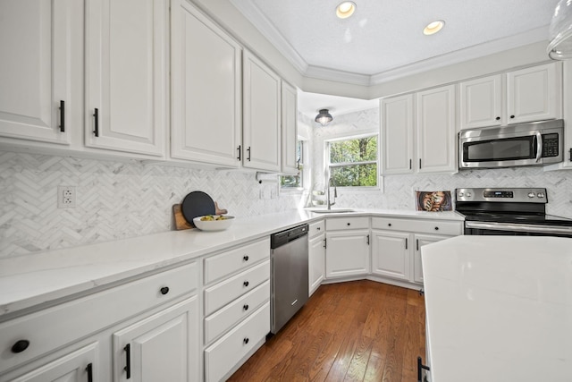 kitchen with a sink, tasteful backsplash, white cabinetry, ornamental molding, and appliances with stainless steel finishes