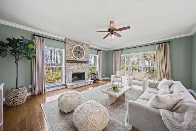 living room featuring crown molding, ceiling fan, baseboards, a fireplace, and wood finished floors