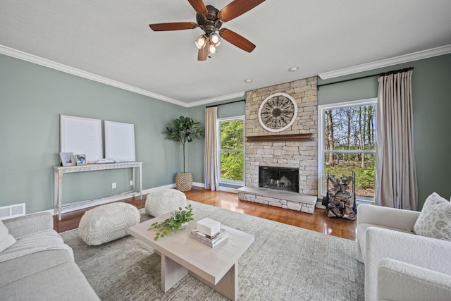 living room with visible vents, ornamental molding, a fireplace, wood finished floors, and a ceiling fan
