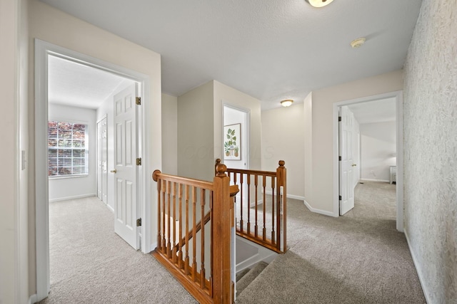 hall with an upstairs landing, carpet flooring, and baseboards