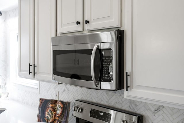 interior details with stainless steel microwave, decorative backsplash, and white cabinets