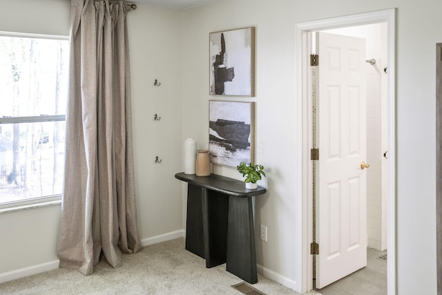 hallway featuring baseboards, light carpet, and plenty of natural light