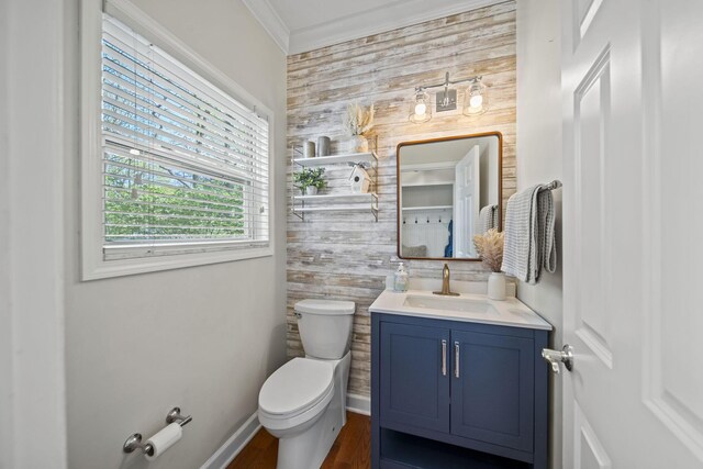 half bathroom featuring baseboards, toilet, ornamental molding, wood finished floors, and vanity