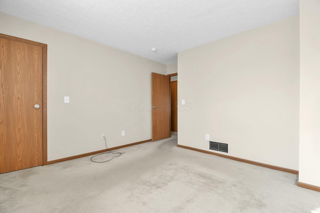 spare room with a textured ceiling, visible vents, baseboards, and light carpet