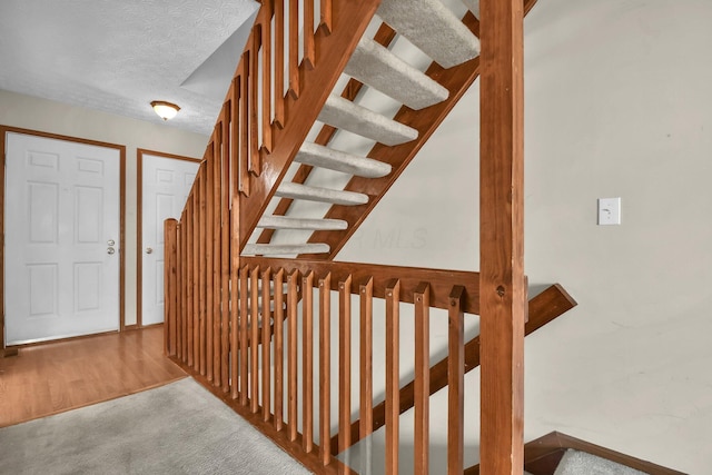 stairway with carpet floors and a textured ceiling