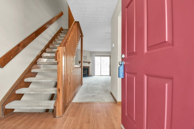 entryway with stairway, a fireplace, a textured ceiling, and light wood-style floors