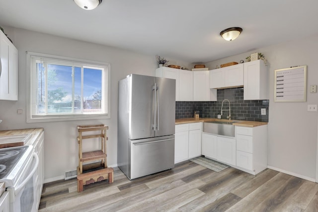 kitchen with a sink, white electric range, wood counters, backsplash, and freestanding refrigerator