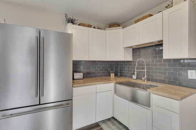 kitchen featuring butcher block counters, decorative backsplash, freestanding refrigerator, white cabinets, and a sink