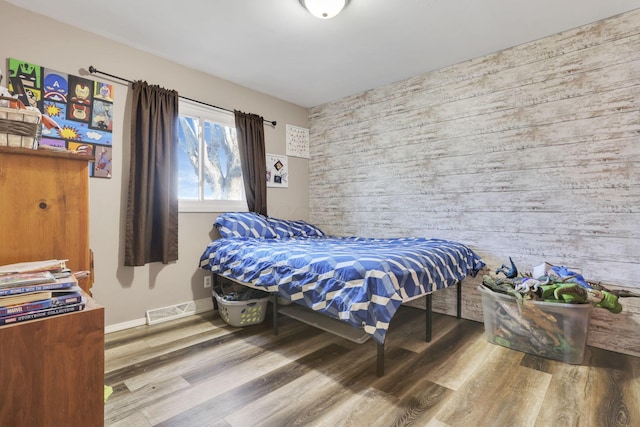 bedroom with visible vents, baseboards, wooden walls, and wood finished floors