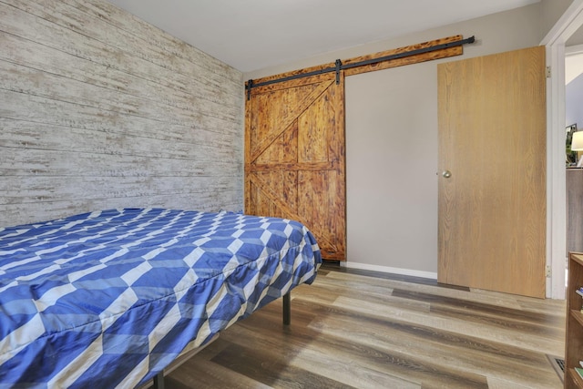 bedroom featuring a barn door, baseboards, wooden walls, and wood finished floors