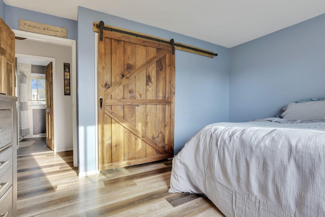 bedroom with a barn door, baseboards, and light wood-style floors