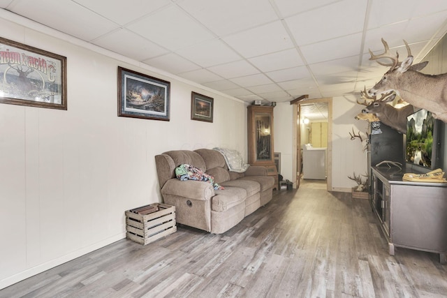 living area featuring a paneled ceiling, light wood-type flooring, washer / clothes dryer, and baseboards