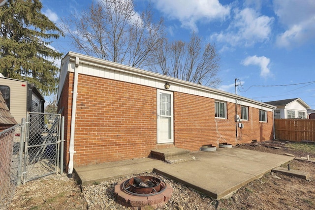 back of property featuring fence, an outdoor fire pit, entry steps, a patio area, and brick siding