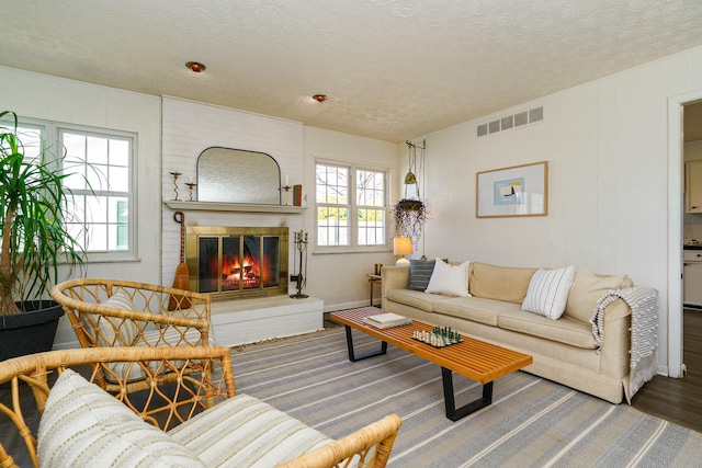 living area featuring visible vents, a brick fireplace, a textured ceiling, and wood finished floors