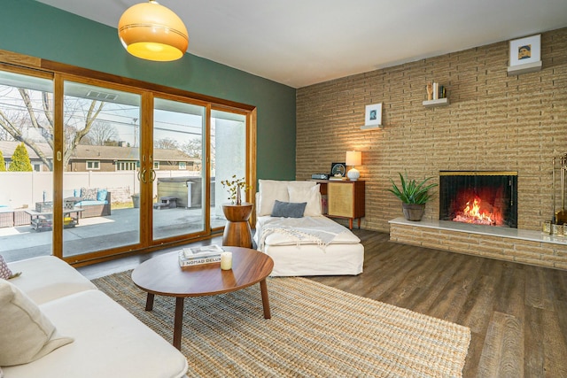 living area featuring a brick fireplace, brick wall, and wood finished floors