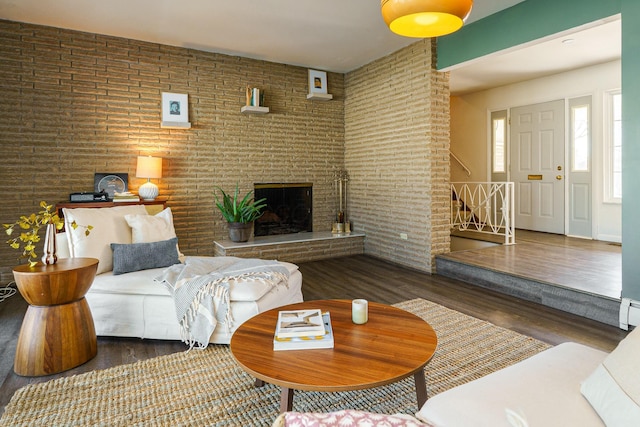 living area featuring wood finished floors, brick wall, a baseboard radiator, a brick fireplace, and stairs