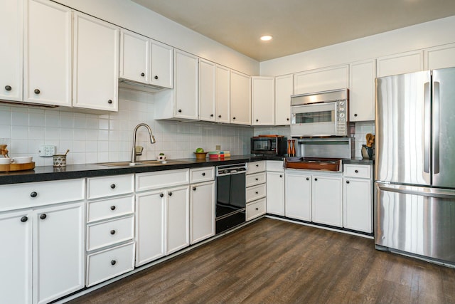 kitchen featuring black appliances, a sink, dark countertops, dark wood-style floors, and white cabinets