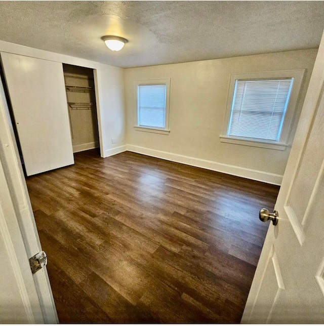 unfurnished bedroom with dark wood finished floors, baseboards, a closet, and a textured ceiling