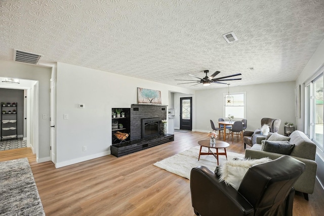 living area featuring a brick fireplace, visible vents, light wood-type flooring, and baseboards