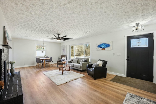 living room featuring light wood-type flooring, baseboards, a textured ceiling, and a fireplace