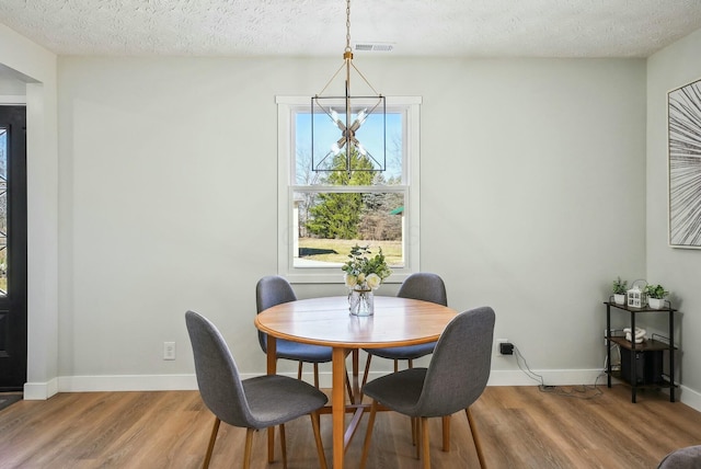 dining area with visible vents, a textured ceiling, light wood-type flooring, and baseboards