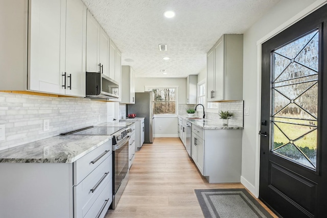 kitchen with light wood finished floors, appliances with stainless steel finishes, light stone countertops, and a sink