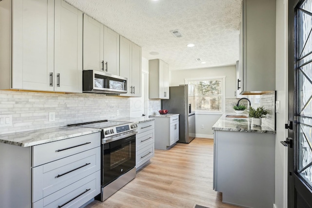 kitchen with visible vents, a sink, light wood-style floors, appliances with stainless steel finishes, and light stone countertops