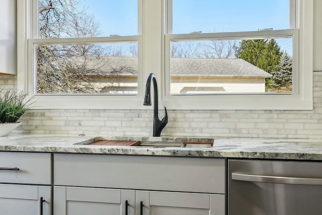 interior details featuring light stone counters, a sink, white cabinets, and stainless steel dishwasher