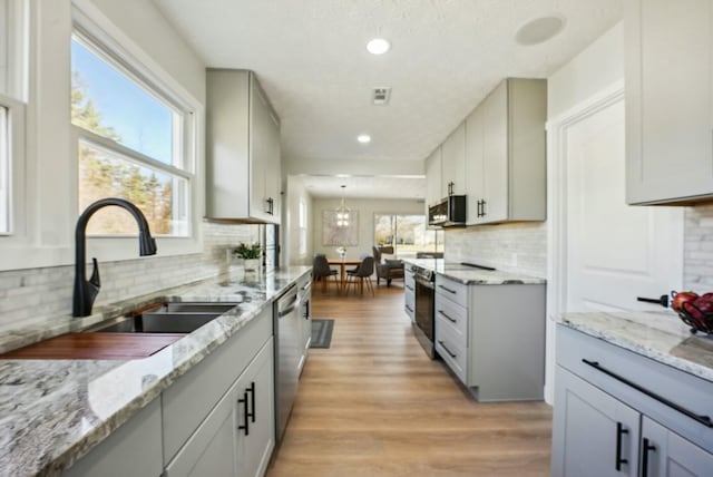 kitchen with light stone countertops, light wood-style flooring, gray cabinets, stainless steel appliances, and a sink