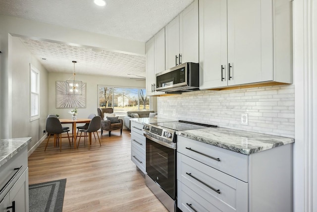 kitchen featuring backsplash, light stone counters, appliances with stainless steel finishes, light wood-style floors, and a textured ceiling