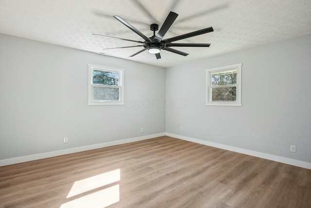 unfurnished room featuring a wealth of natural light, a textured ceiling, baseboards, and wood finished floors