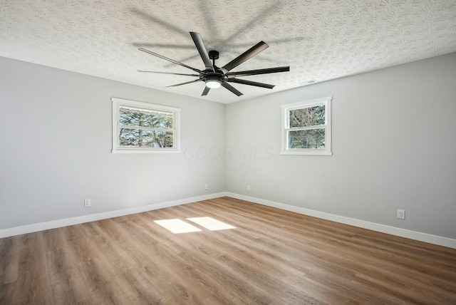 spare room featuring wood finished floors, a healthy amount of sunlight, baseboards, and a textured ceiling