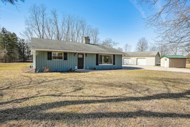 view of front of home with board and batten siding, a detached garage, a front lawn, a chimney, and an outbuilding