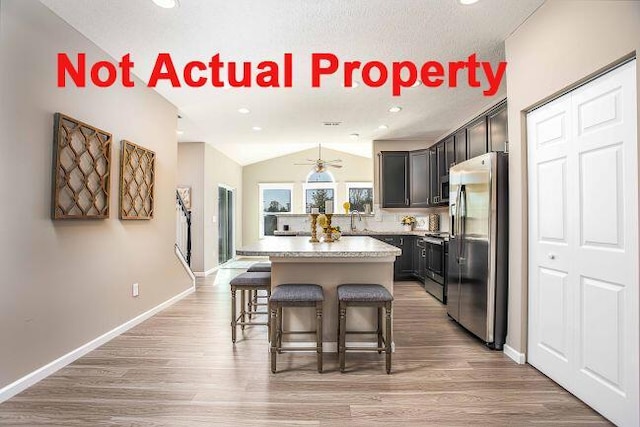 kitchen with a kitchen island, a breakfast bar area, light wood-type flooring, lofted ceiling, and appliances with stainless steel finishes