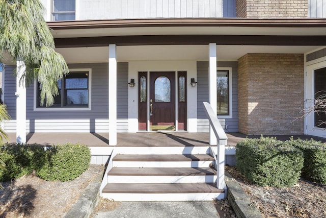 view of exterior entry featuring covered porch and brick siding