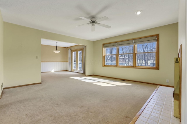 empty room with light carpet, a wainscoted wall, baseboards, and ceiling fan