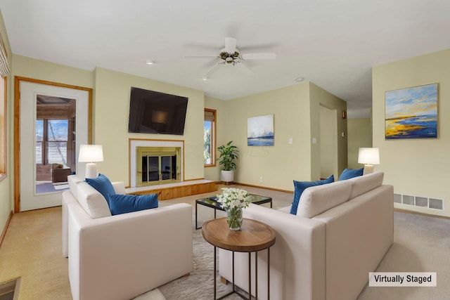 living area featuring visible vents, ceiling fan, baseboards, light carpet, and a glass covered fireplace